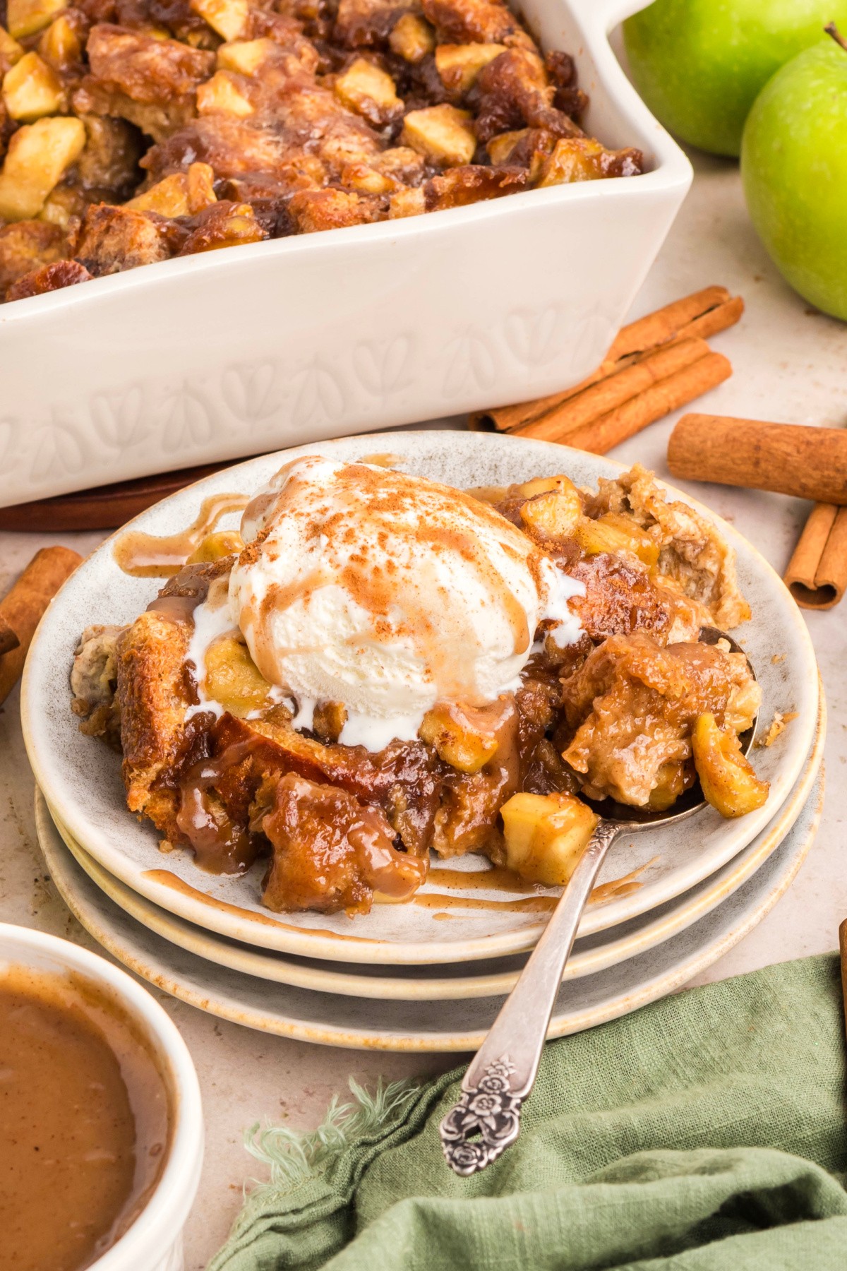 Brioche apple dessert with caramel drizzle and melting vanilla ice cream. Warm brioche apple dessert topped with vanilla ice cream and rich caramel sauce, surrounded by cinnamon sticks and green apples.