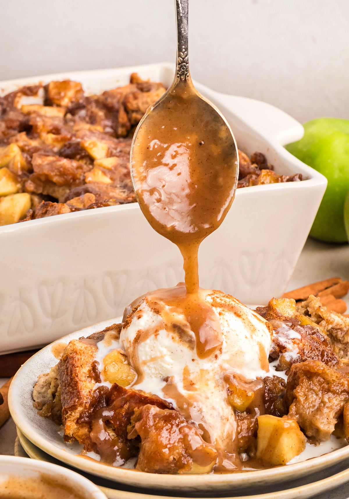 Pouring caramel sauce over warm bread pudding with vanilla ice cream. Spoon drizzling caramel sauce over warm bread pudding topped with vanilla ice cream, showing the rich texture and glossy finish.