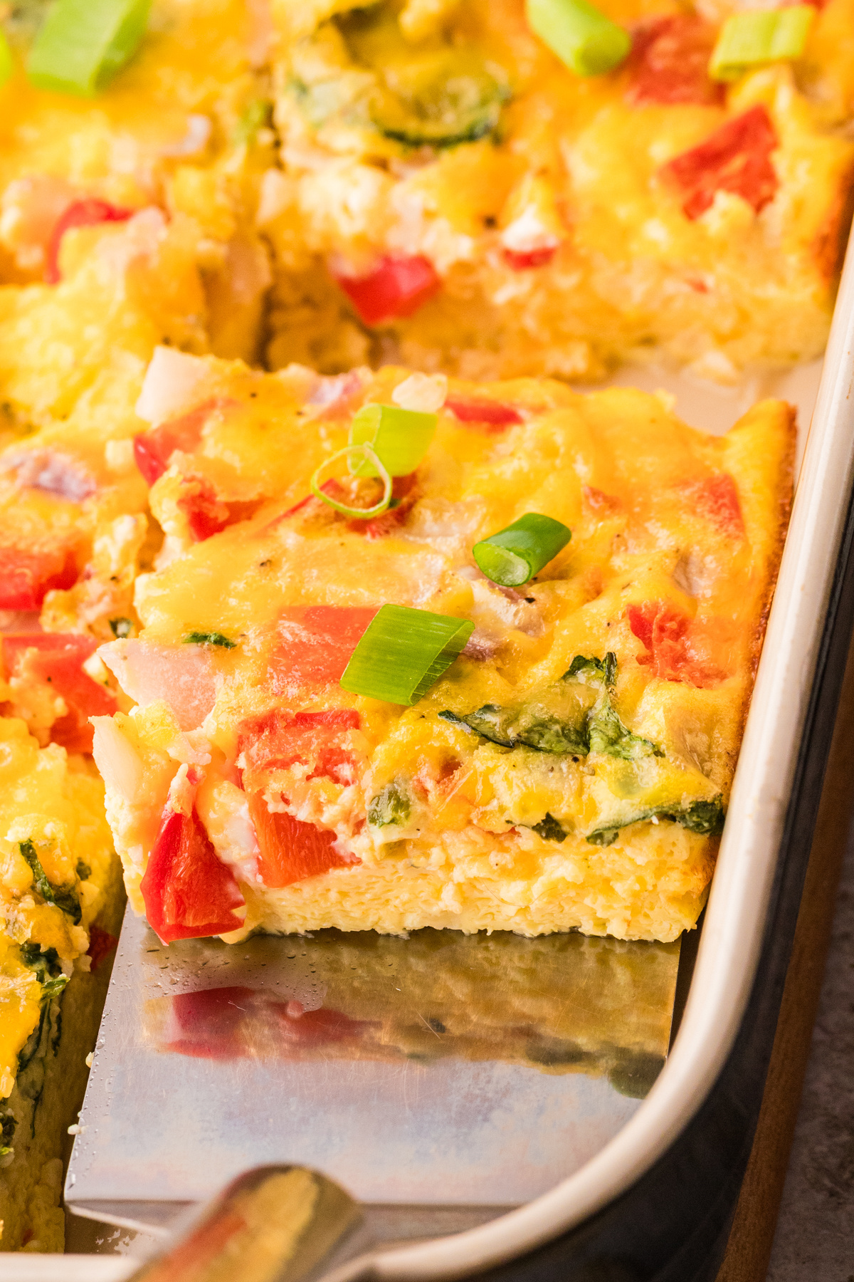 High protein cottage cheese egg bake with cheddar, peppers, and spinach on spatula