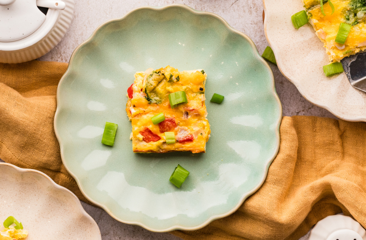 Cottage cheese breakfast casserole square on a green plate with green onion garnish
