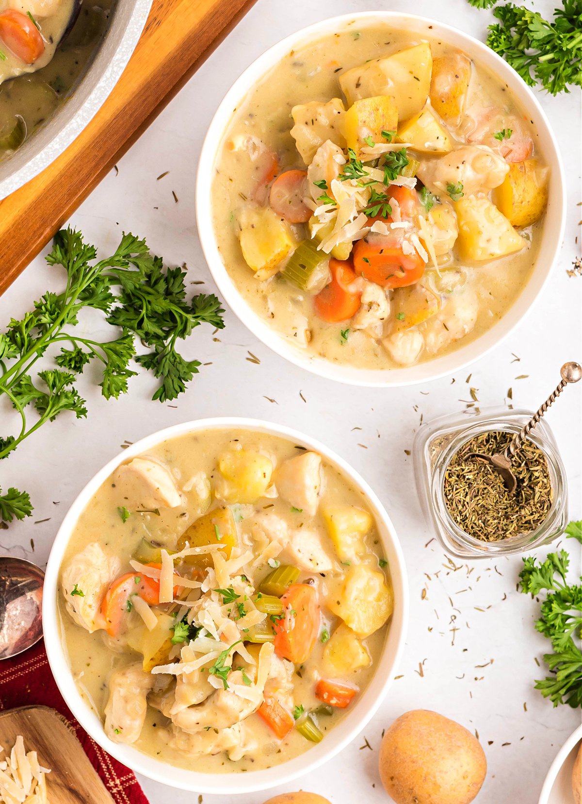 creamy chicken stew in white bowls with potatoes, carrots, and celery in a rich broth, topped with parsley and Parmesan.