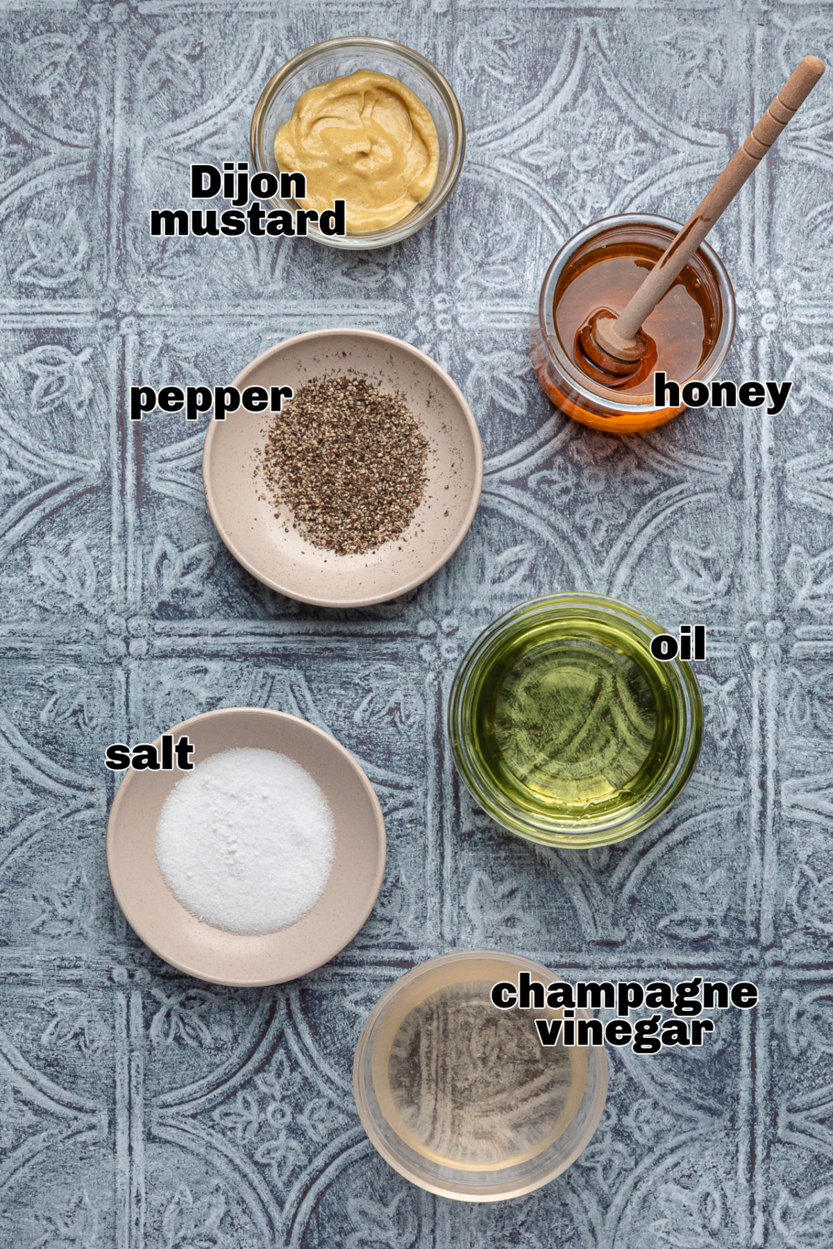 Ingredients for honey champagne vinaigrette on a blue surface, including Dijon mustard, honey, oil, champagne vinegar, salt, and pepper.
