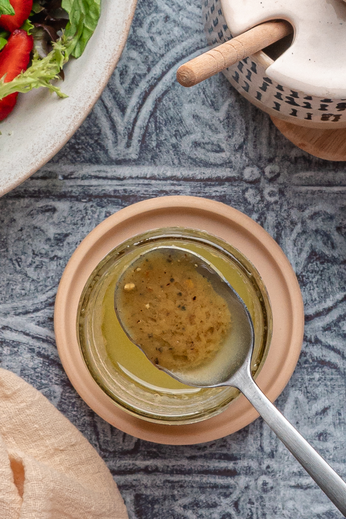 Spoonful of homemade Dijon and honey dressing lifted from a glass jar on a textured blue surface.