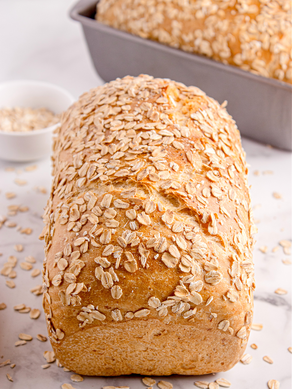 honey oatmeal bread fresh from the oven Golden loaf of honey oatmeal bread topped with oats on a marble surface.