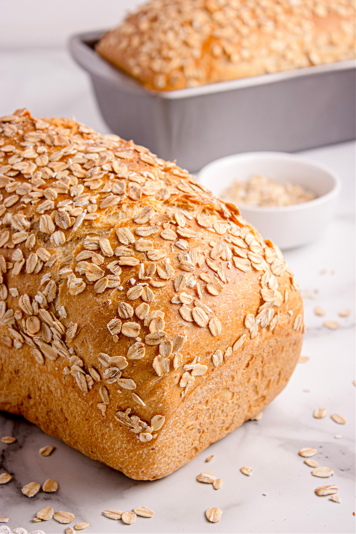 soft honey oat bread loaves Two loaves of soft honey oat bread topped with oats cooling beside a small bowl of oats.