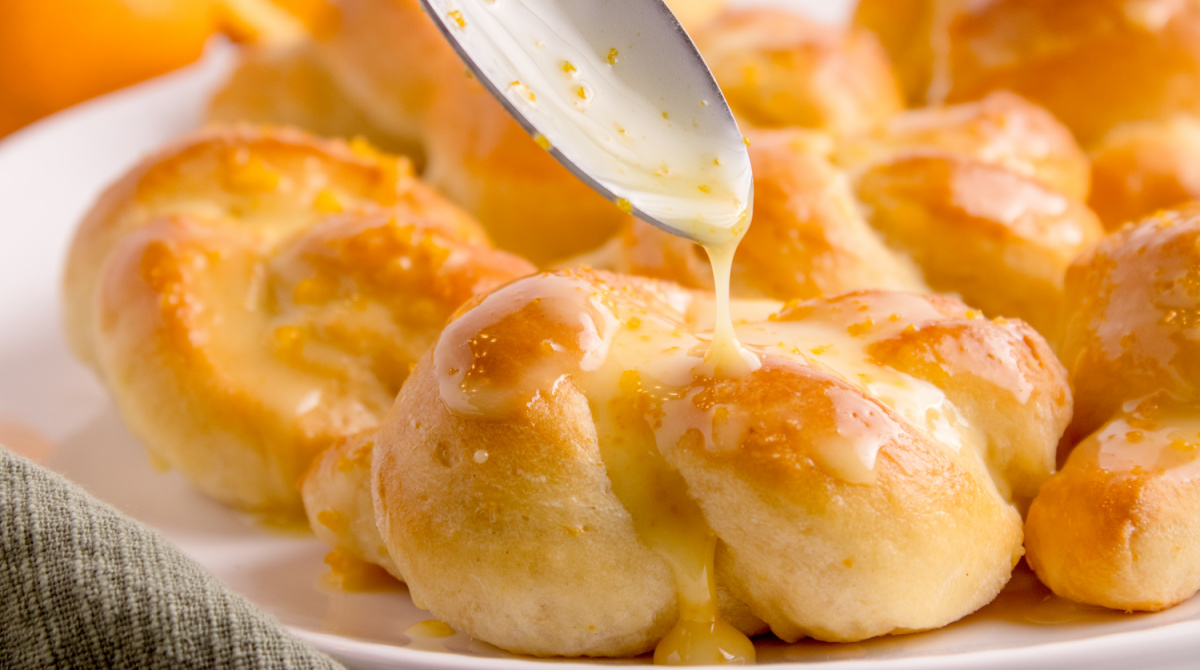Orange Glaze Drizzle on Sweet Rolls Spoon drizzling orange glaze over freshly baked rolls.