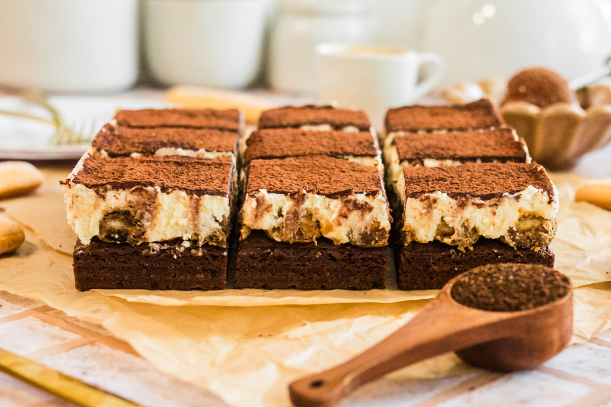 tiramisu brownies easy espresso dessert baked and sliced on parchment. tray of tiramisu brownies with rich cocoa dusting and creamy mascarpone layers.