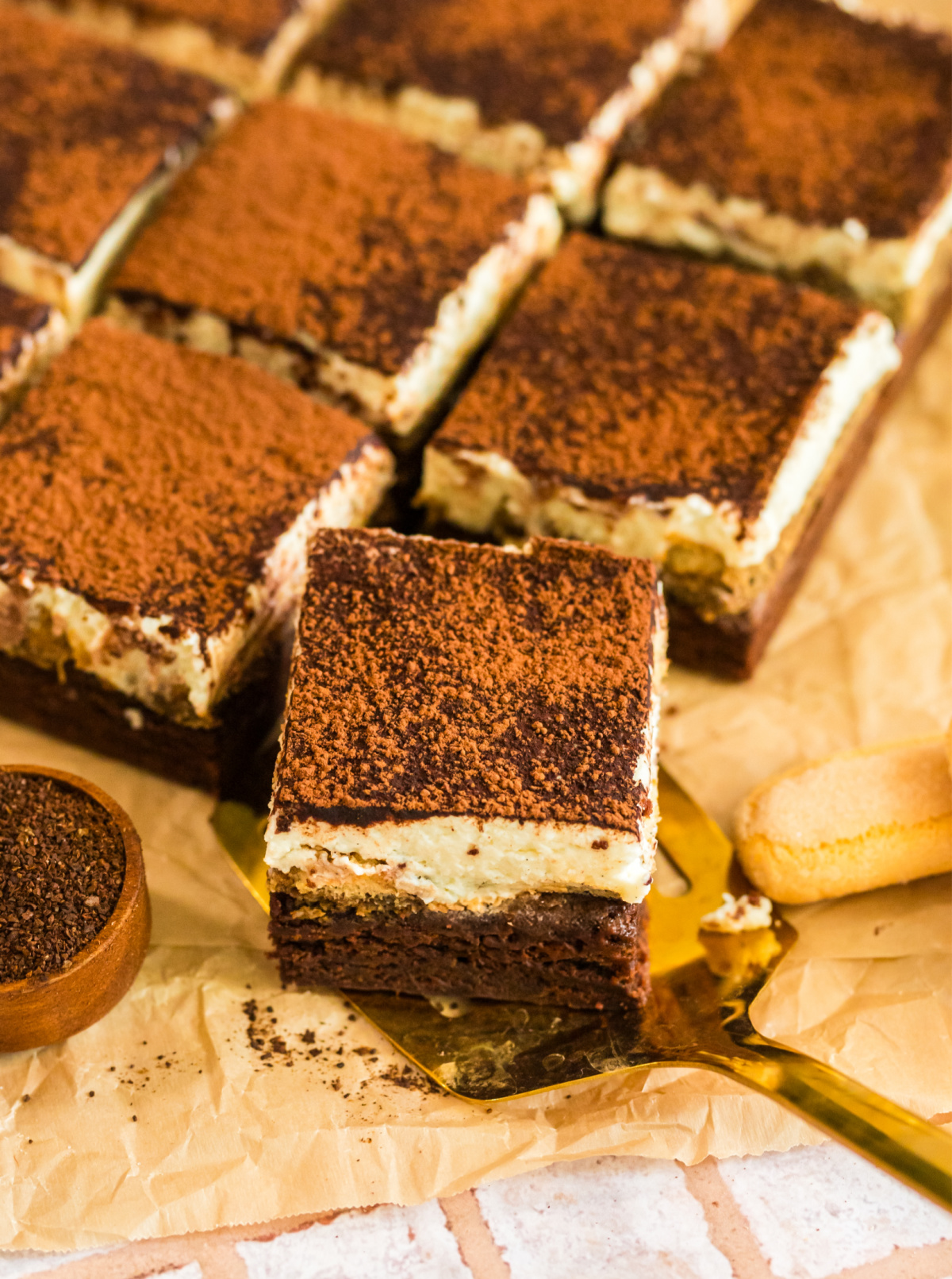 tiramisu brownies cut dessert squares with cocoa layer and mascarpone filling. tiramisu brownies cut into squares topped with cocoa powder, served on parchment paper.