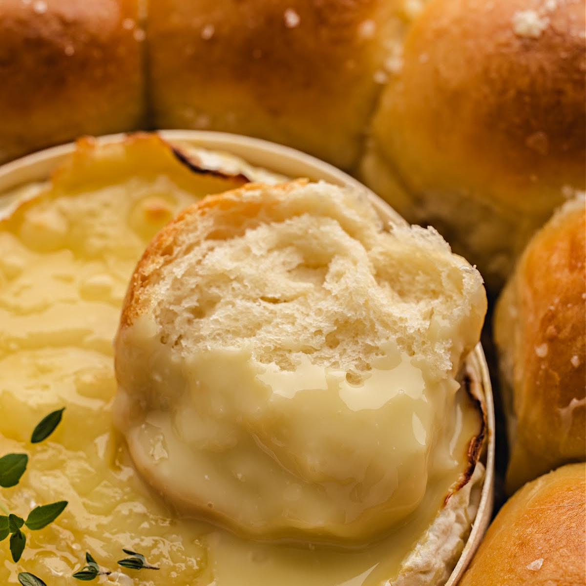 A soft pull-apart roll dipped into molten Camembert, showing the stretchy, glossy cheese clinging to the warm bread.