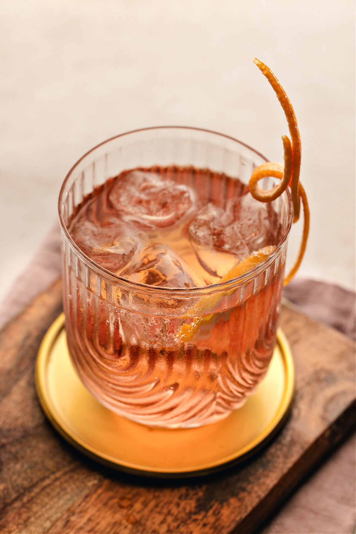 A chilled Lillet Rosé spritz glowing pale pink in a textured glass, served over ice with a long curled grapefruit twist resting on the rim.