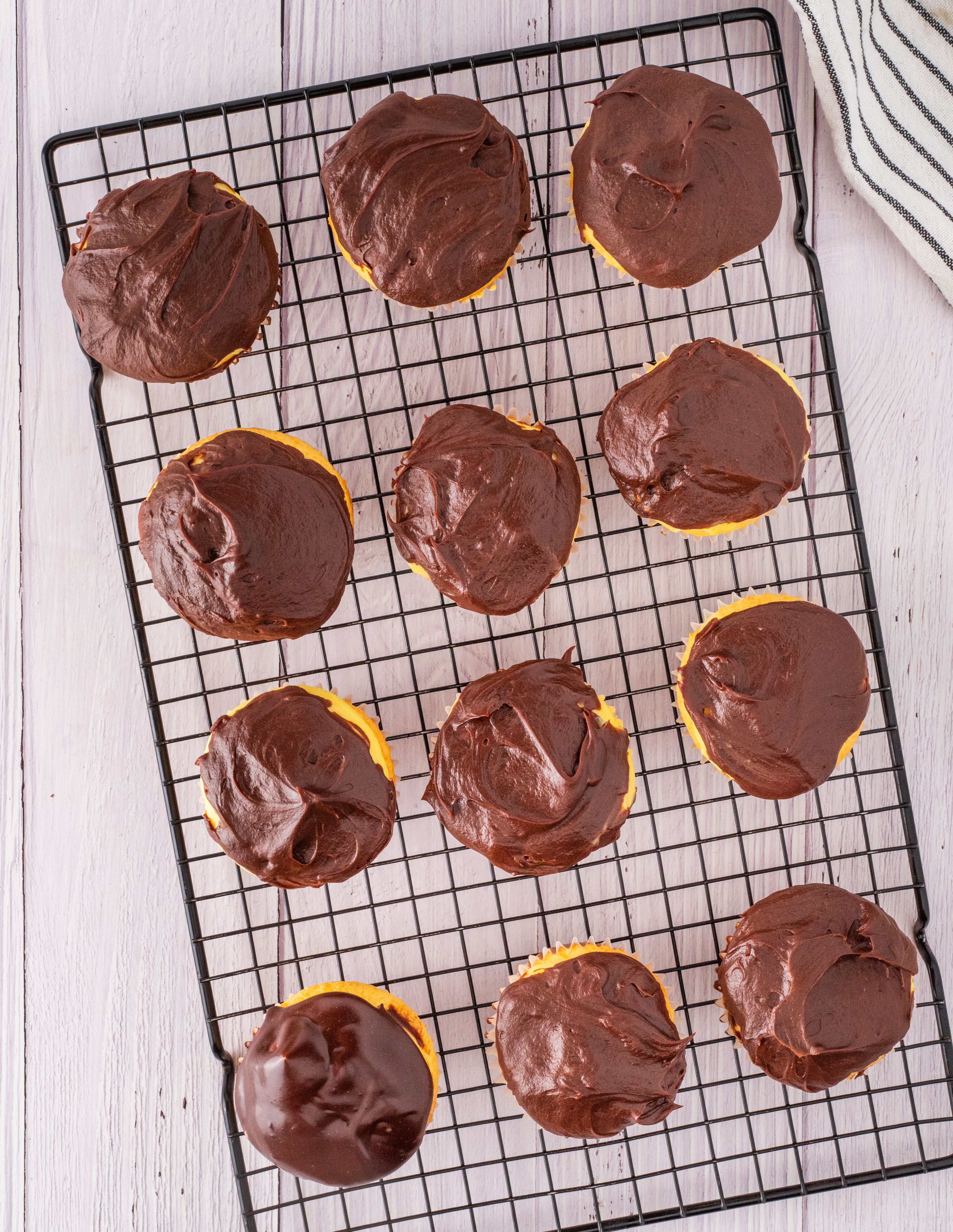 Cupcakes with Chocolate Ganache on Cooling Rack Freshly frosted cupcakes with chocolate ganache cooling on a wire rack, showing the thick glossy layer set over vanilla cream centers
