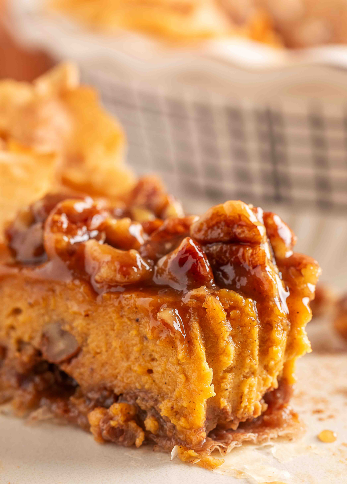 A close-up slice of pumpkin praline pie with a crunchy brown-sugar pecan layer on top, showing the soft pumpkin custard interior and flaky phyllo crust. The glossy praline topping highlights the caramelized sugars and chopped pecans for texture contrast.