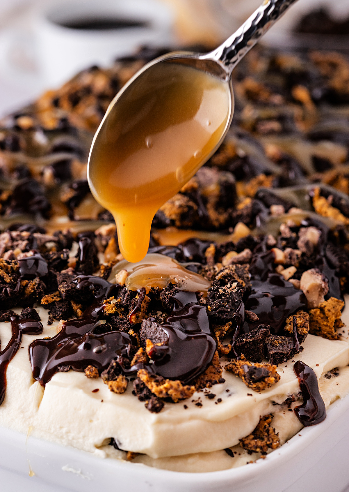 Caramel being drizzled over a layered espresso and mascarpone dessert topped with crushed Toffee Crunch OREOs and chocolate sauce.