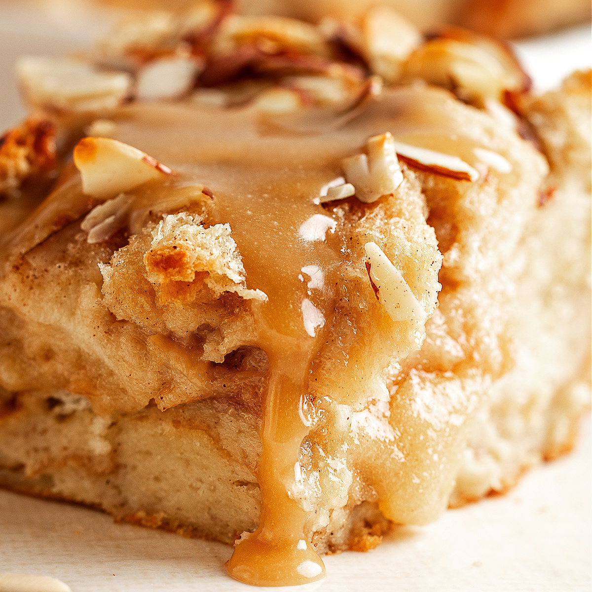 A slice of almond cream bread pudding with brown sugar glaze dripping down the sides, showing its soft, custardy center.