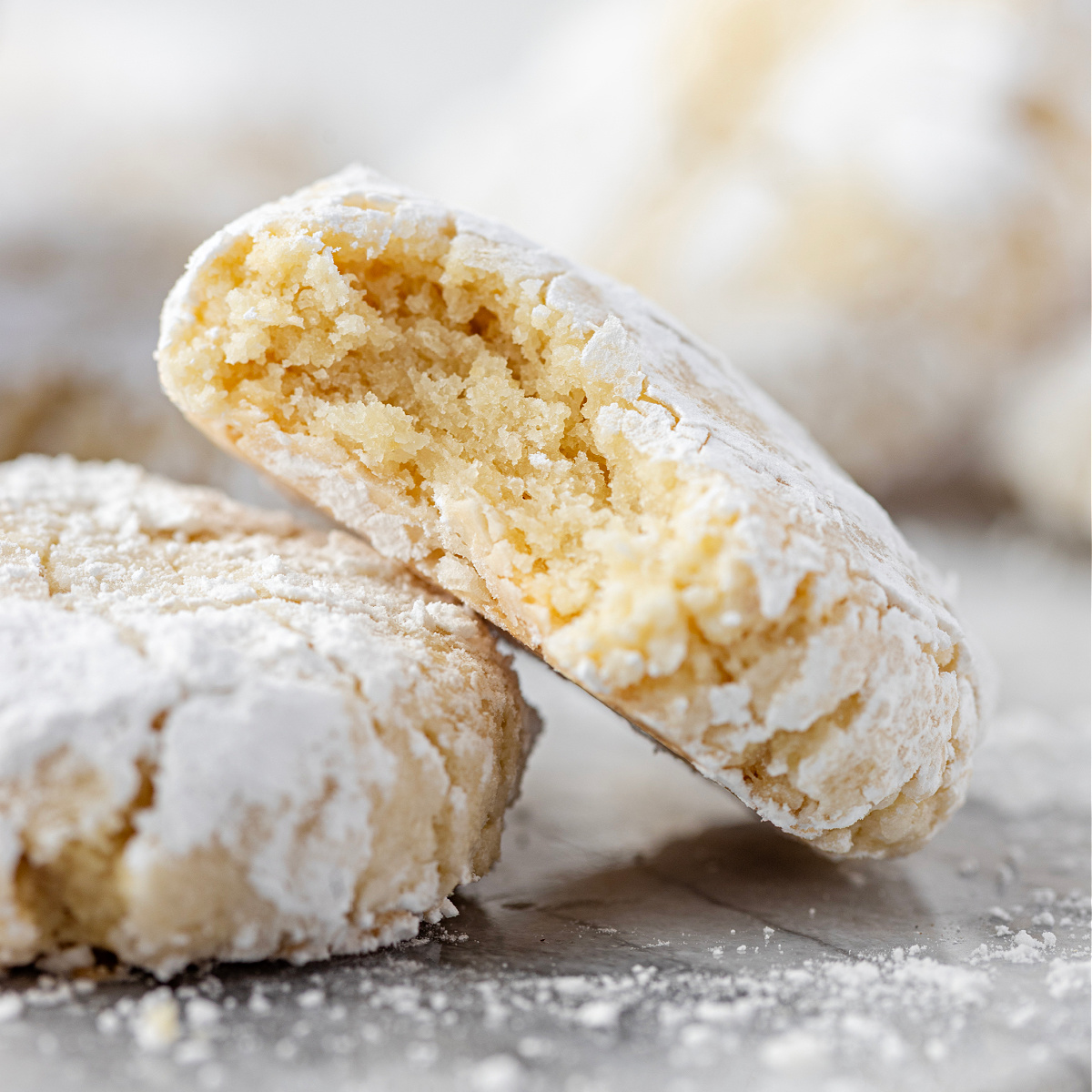 Amaretti Cookie A soft, crackled almond cookie broken open on a marble surface, showing its tender interior.