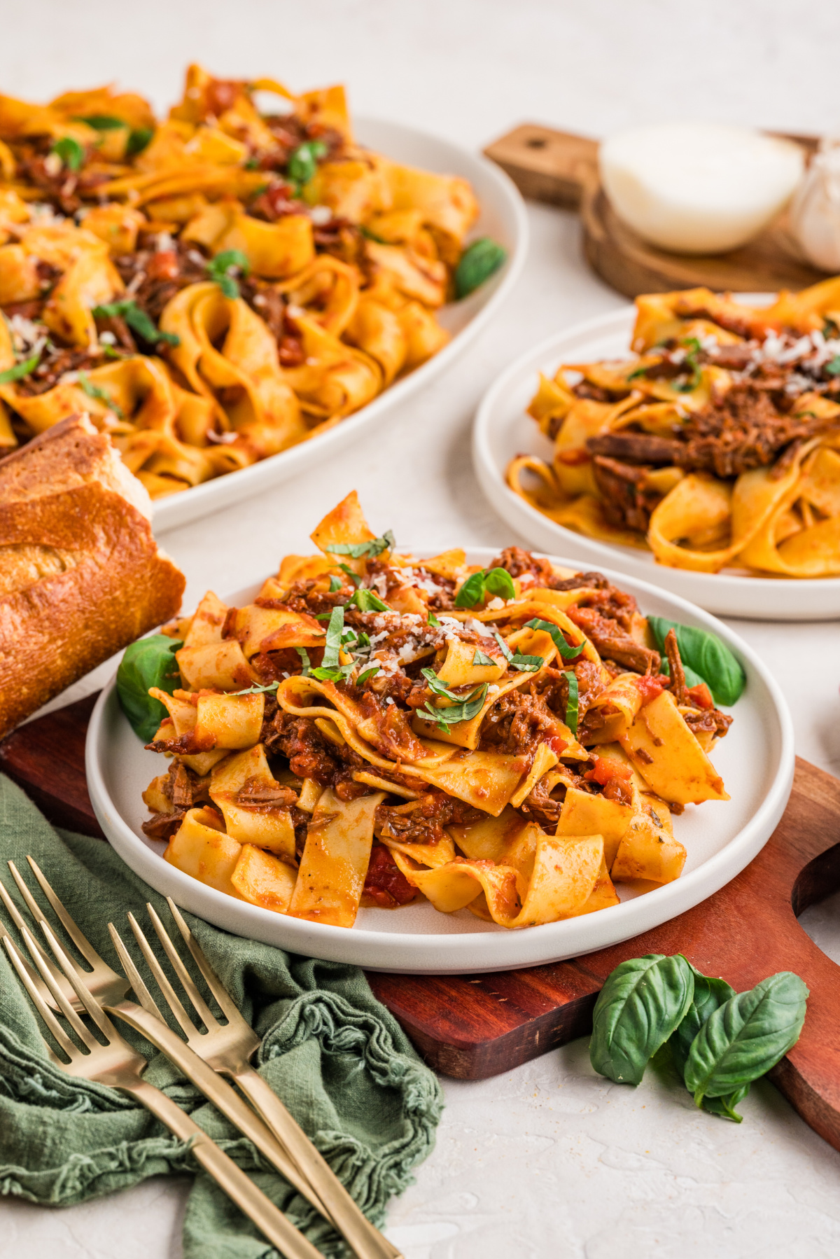 Plated servings of pappardelle with slow-cooked beef ragù and fresh herbs. Plates of pappardelle tossed with tender shredded beef ragù, served with fresh basil and crusty bread, ready at the table.
