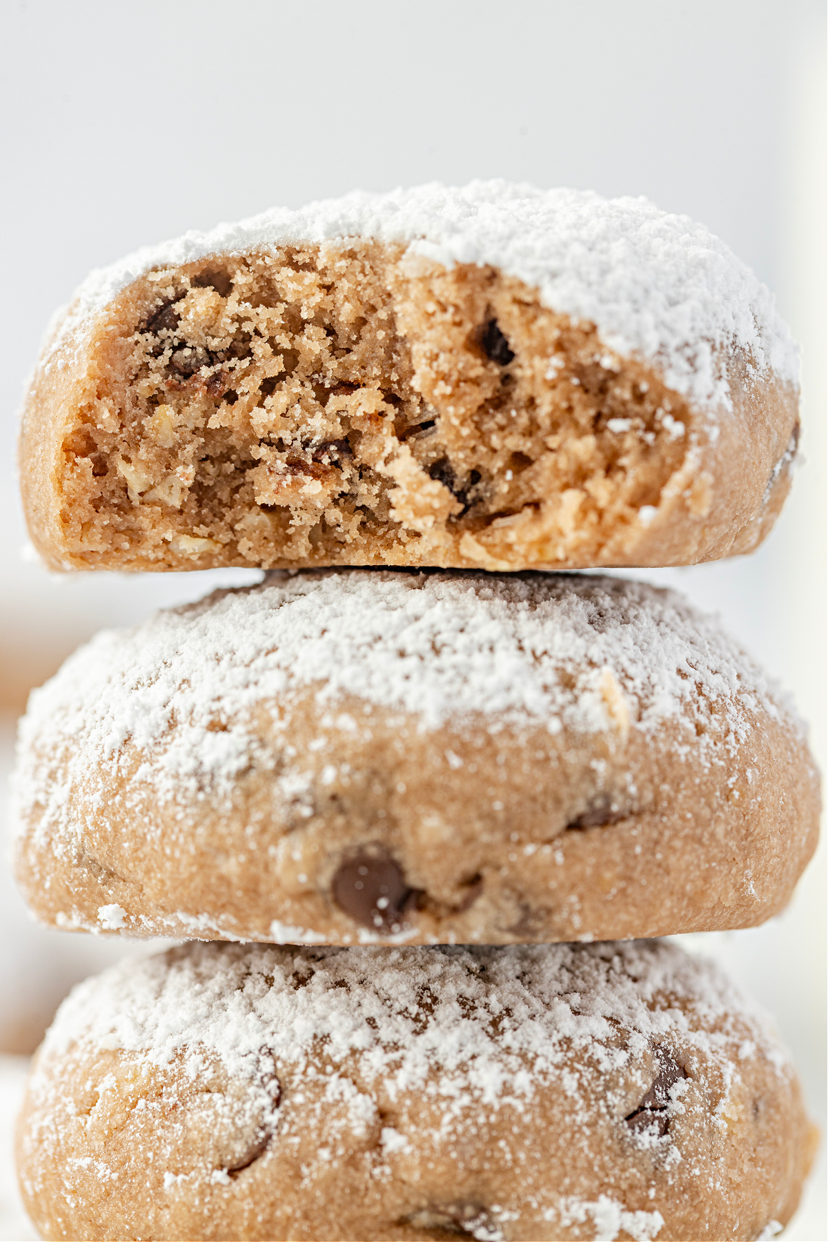A close-up of a bitten cookie highlighting the crumb and chocolate chips. A bitten Danish wedding cookie stacked over two others, showing the soft interior and chocolate chip texture.