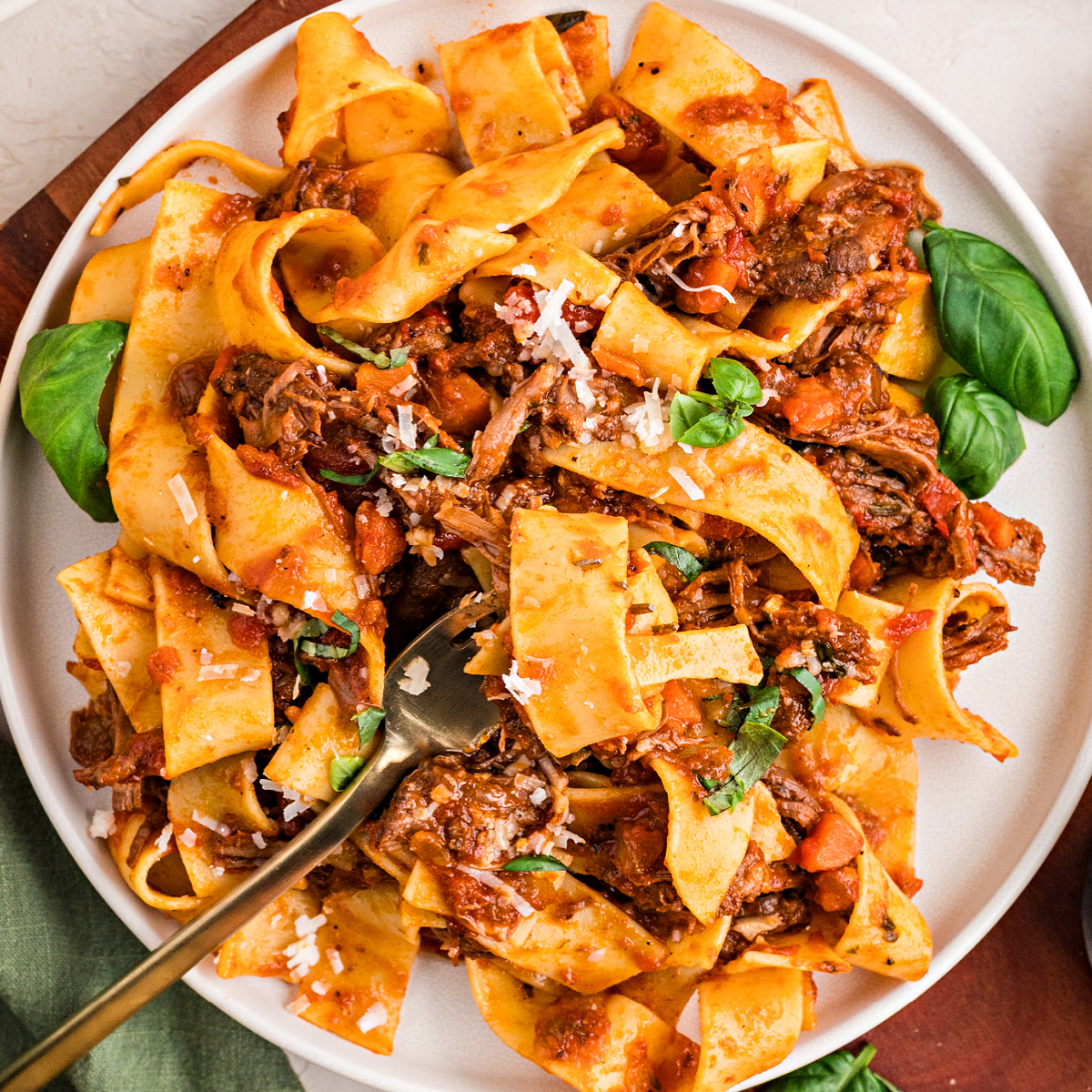 A plate of wide pappardelle coated in tender shredded beef ragù with basil and parmesan, ready to serve.