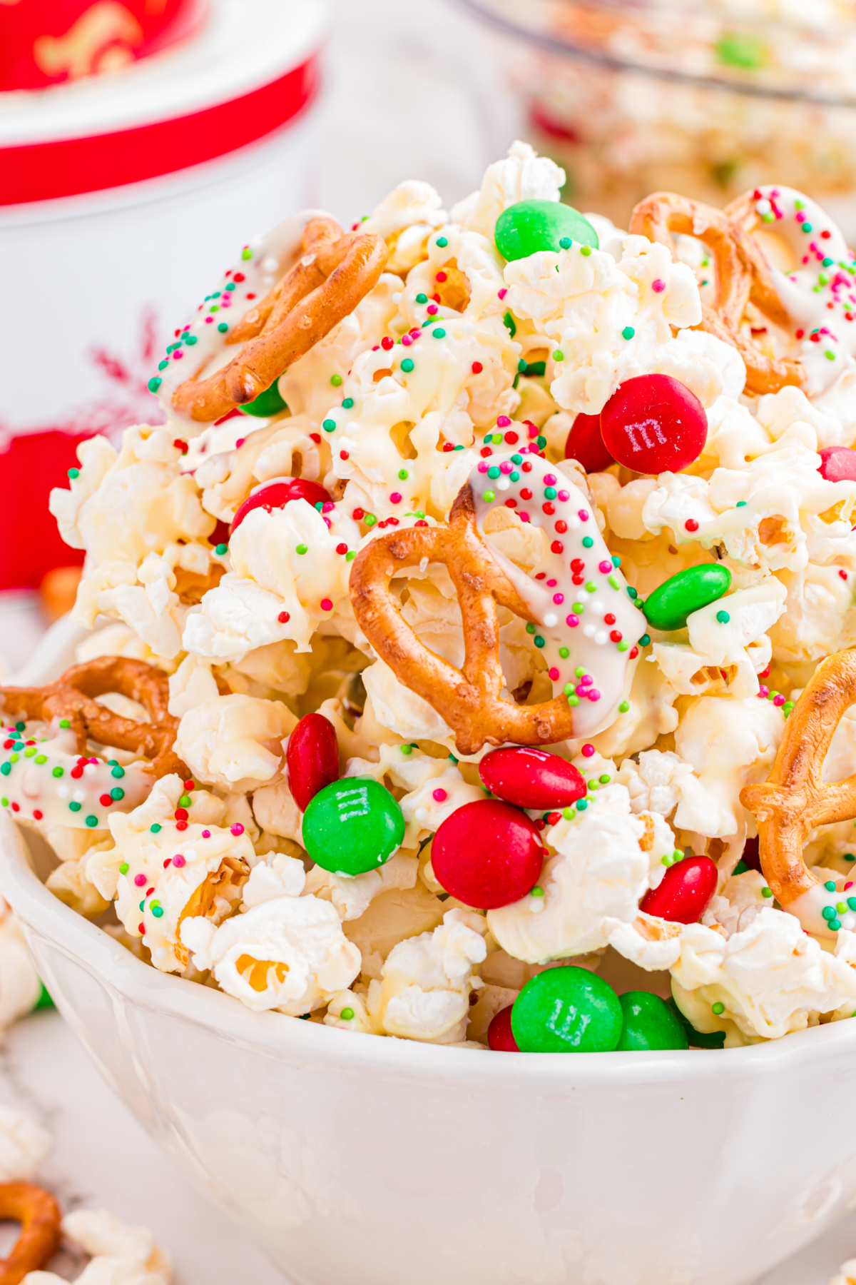 Close-up of Christmas popcorn mix with white chocolate–coated popcorn, pretzels, holiday sprinkles, and candy-coated chocolates.