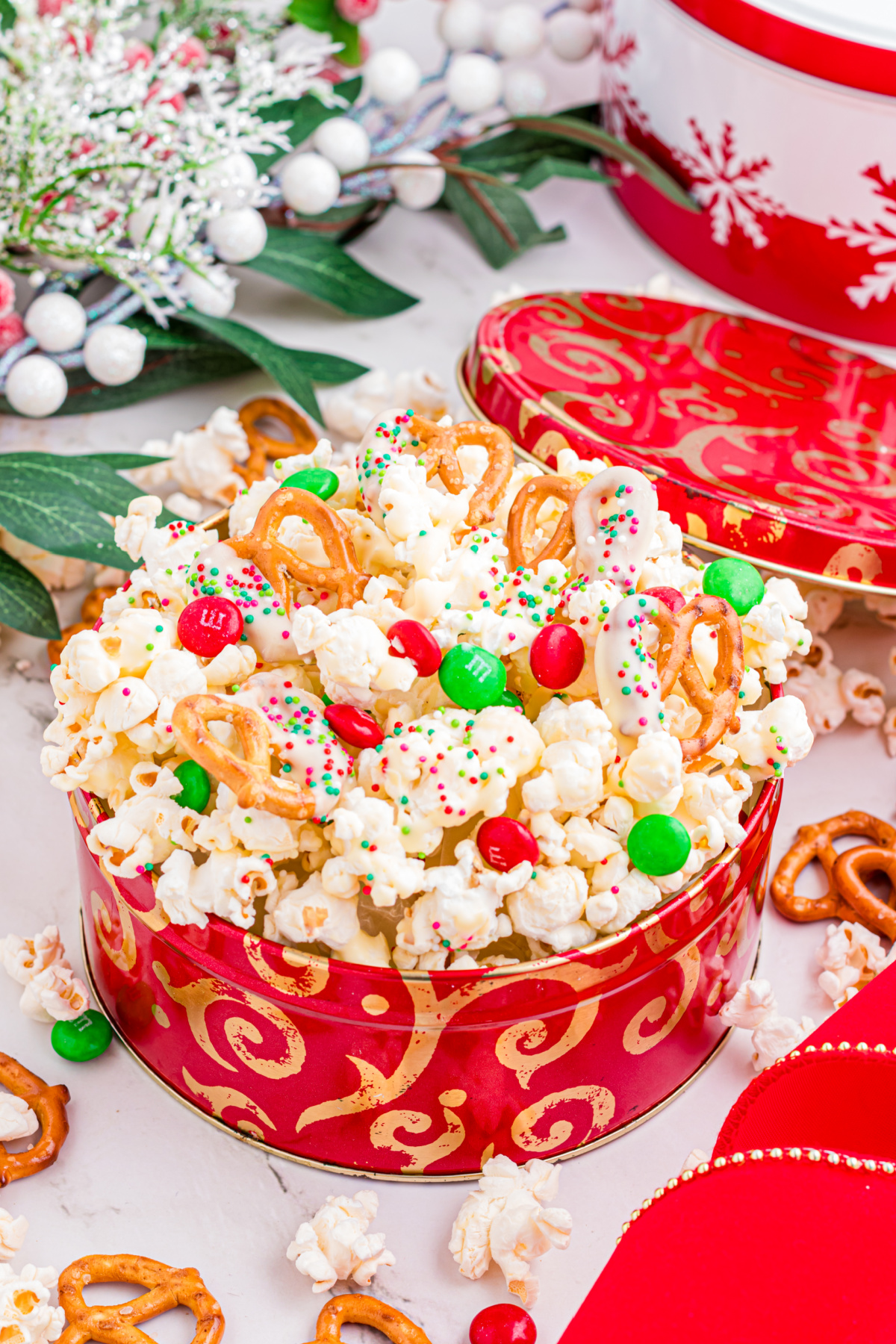White chocolate popcorn with pretzels, holiday M&M’s, and sprinkles piled into a red Christmas tin