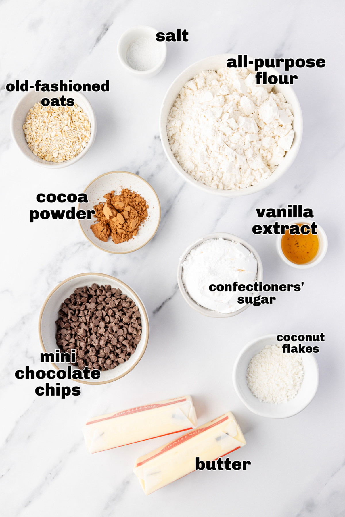 Ingredients laid out before mixing the cookie dough. Danish wedding cookies Measured ingredients arranged on a marble surface, including flour, oats, cocoa powder, chocolate chips, butter, and confectioners’ sugar.