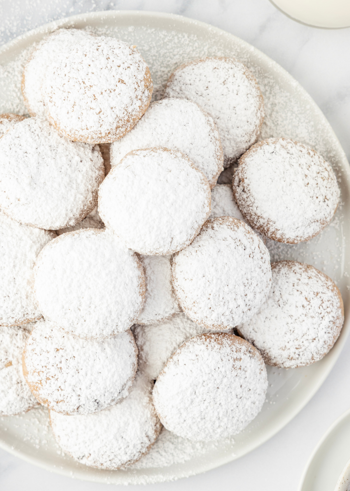 Cookies arranged on a plate beside a cooling rack and milk. A fresh plate of sugar-dusted butter cookies ready to serve.