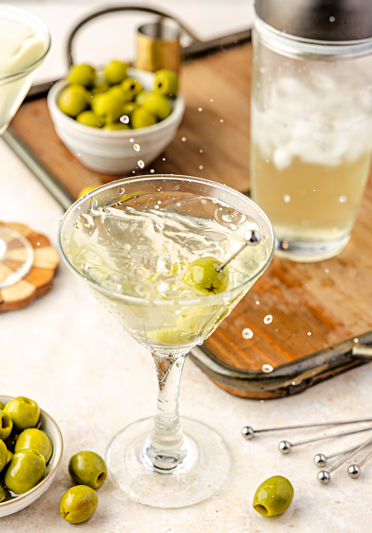 Extra dirty martini poured ice-cold into a stemmed glass with green olives, olive brine, and a shaker on the counter. An extra dirty martini splashing into a chilled glass, finished with green olives and surrounded by olive brine, ice, and bar tools.