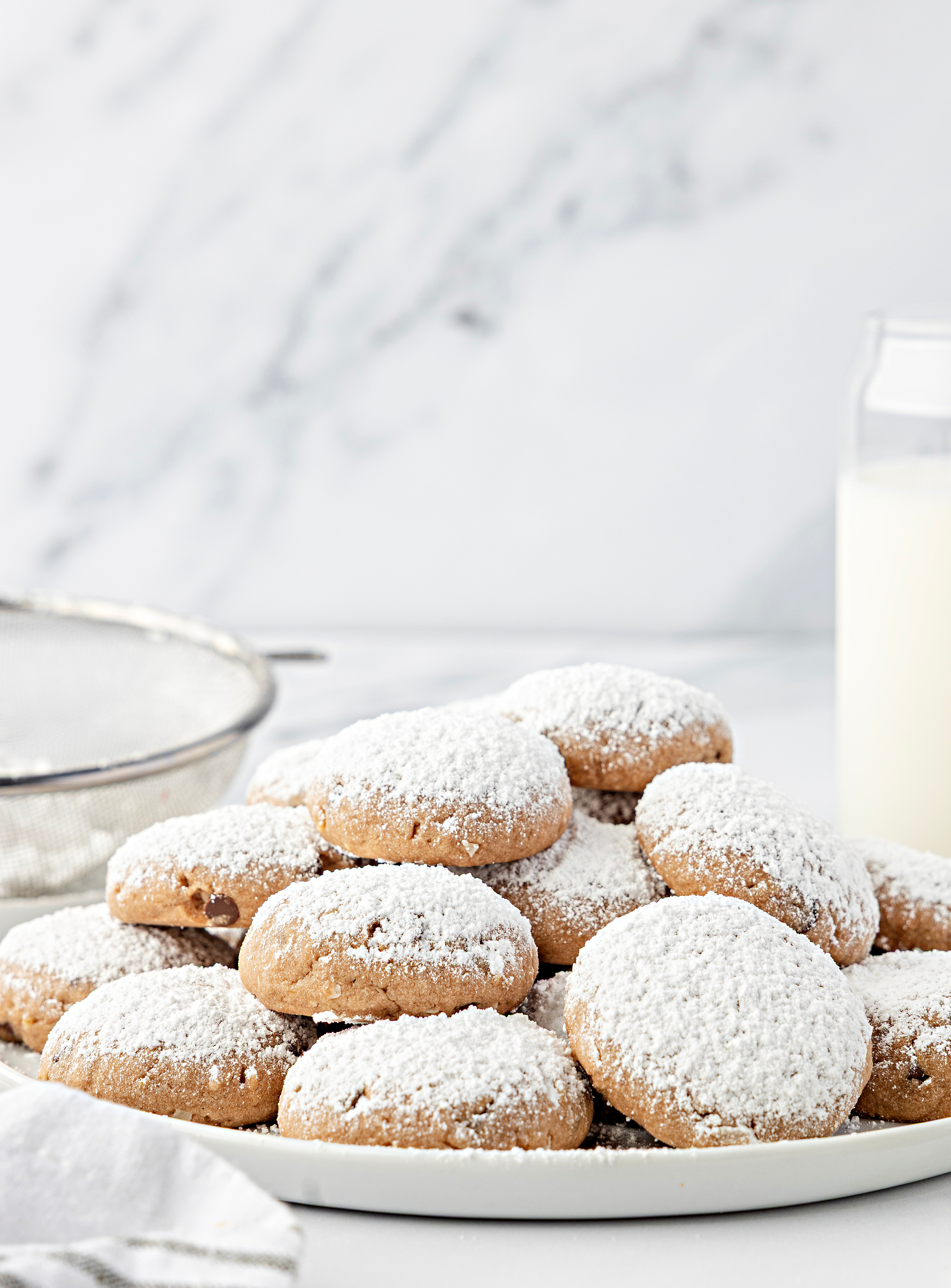 Cookies arranged on a plate beside a cooling rack and milk. An overhead view of soft Danish meltaway cookies on a plate with a thick layer of confectioners’ sugar.
