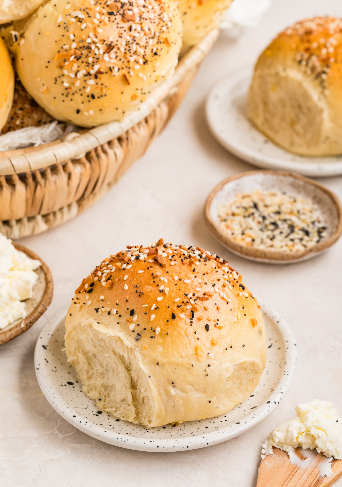 Golden everything bagel rolls with a seasoned crust and tender crumb, photographed whole and partially torn open on a small plate. Everything bagel rolls baked until golden, topped with sesame seeds, poppy seeds, garlic, and onion, with one roll torn open to show the soft, chewy interior.