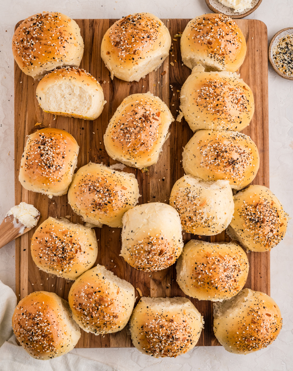 Pull-apart savory rolls baked until golden, shown whole and torn open on a wooden board. Golden baked rolls scattered across a wooden board, some split open to show the soft interior, with everything seasoning sprinkled over the tops.