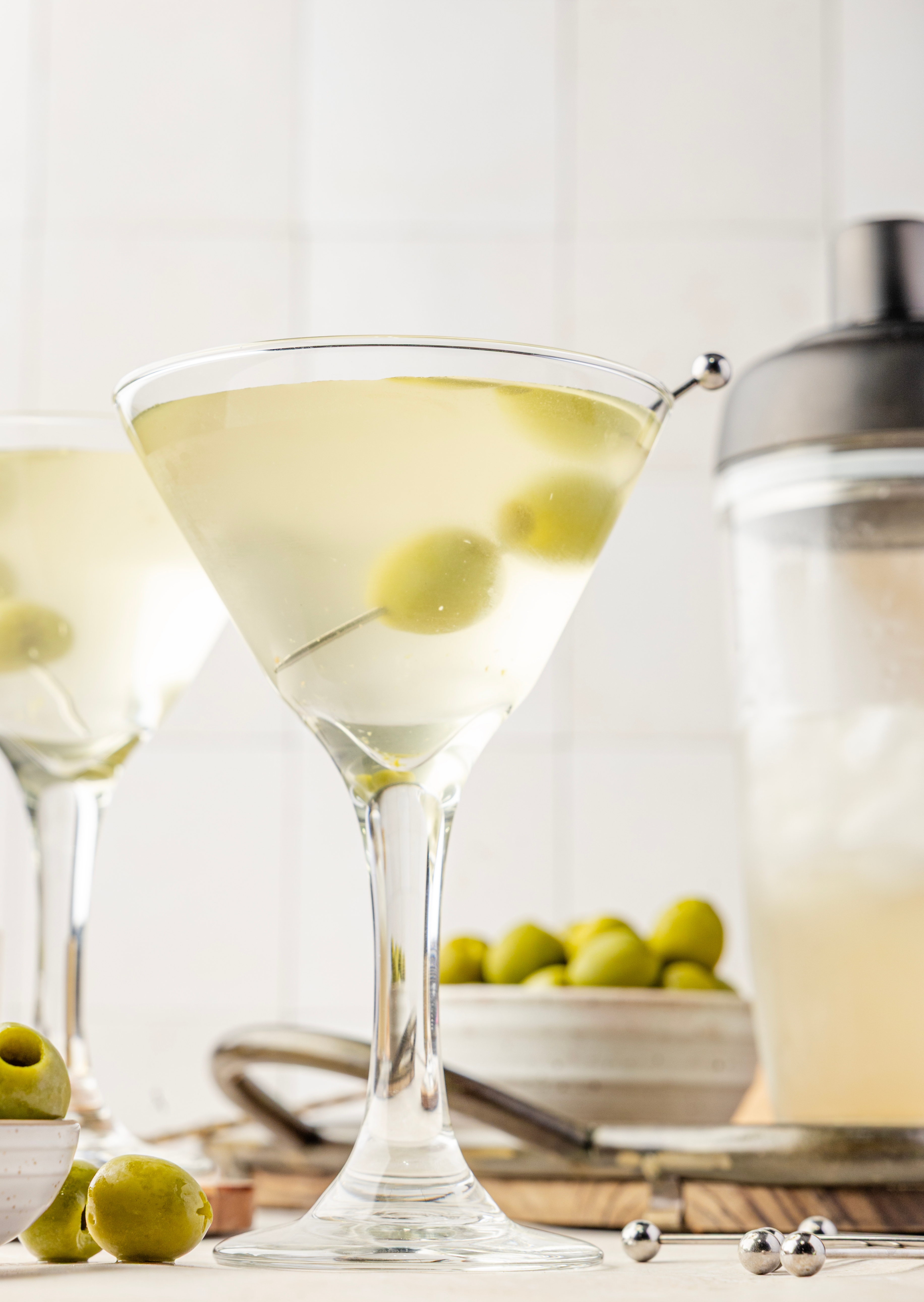 Extra dirty martini with olive garnish served ice-cold on a tray with green olives and bar tools. An extra dirty martini resting on a wooden tray, garnished with two green olives and surrounded by olive brine, ice, and cocktail picks.