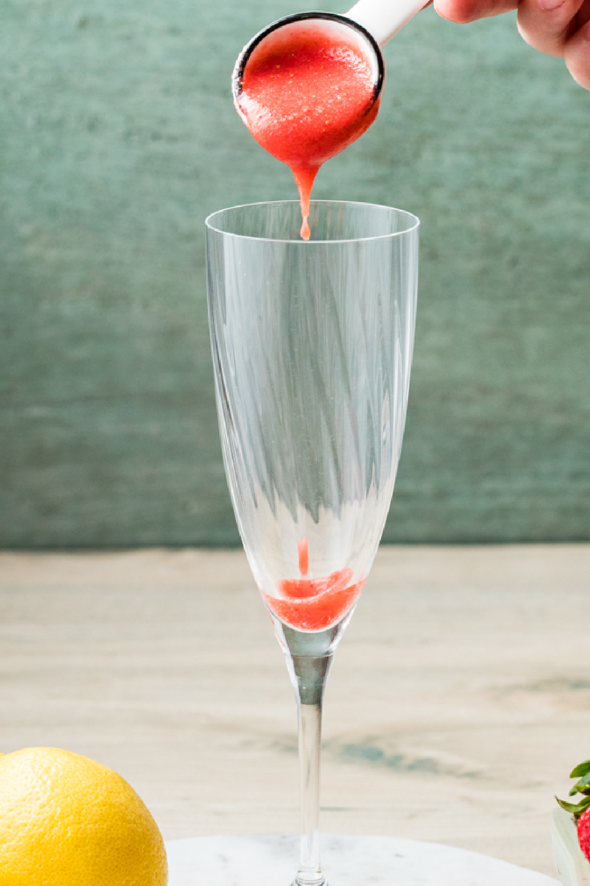 Strawberry purée being spooned into the bottom of a champagne flute.