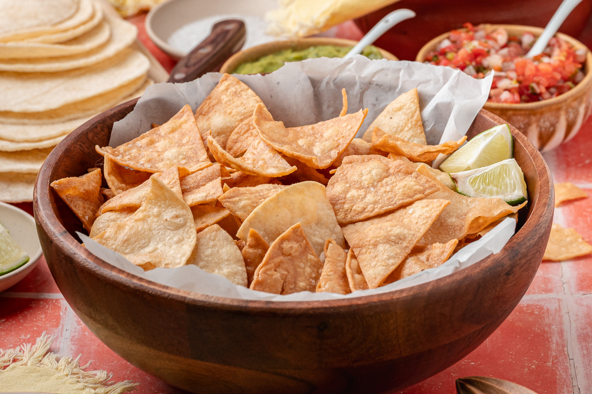 Easy fried tortilla chips served in a wooden bowl A wooden bowl filled with easy fried tortilla chips served with lime wedges and salsa nearby.