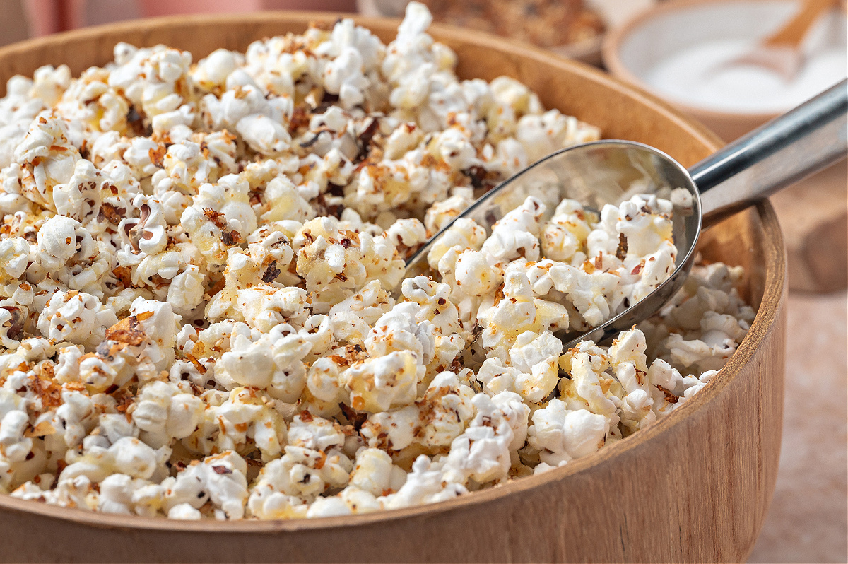 Close-up view of popcorn with a metal scoop in a wooden bowl. A close-up of seasoned popcorn in a wooden bowl, with a metal scoop resting against the side.