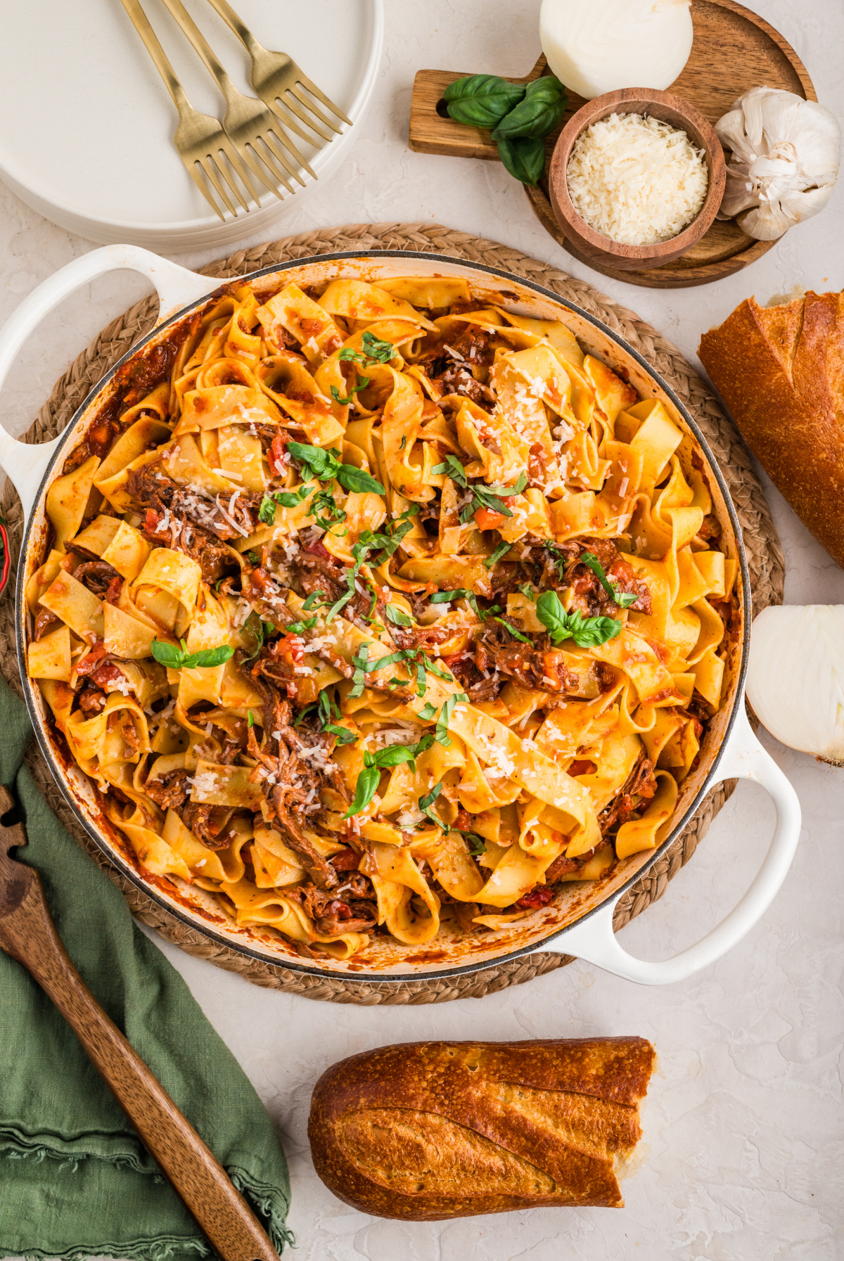 Overhead view of a pot of pappardelle mixed with slow-cooked beef ragù and herbs. A large pot filled with tender shredded beef ragù and wide pappardelle noodles, topped with fresh basil and parmesan, ready to serve with bread.