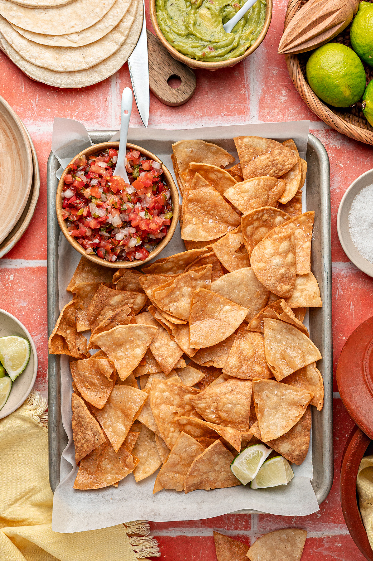Crispy homemade tortilla chips cooling on a sheet pan A sheet pan piled with homemade tortilla chips, golden and blistered, ready for dipping.