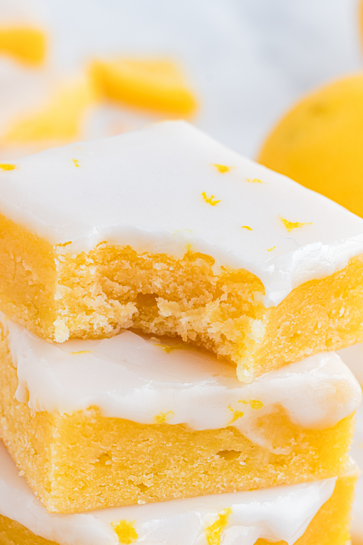 Stacked lemon blondies showing the interior texture and set lemon glaze in detail. Close-up of lemon blondies stacked to show a soft, dense crumb and smooth lemon glaze with fresh zest on top.
