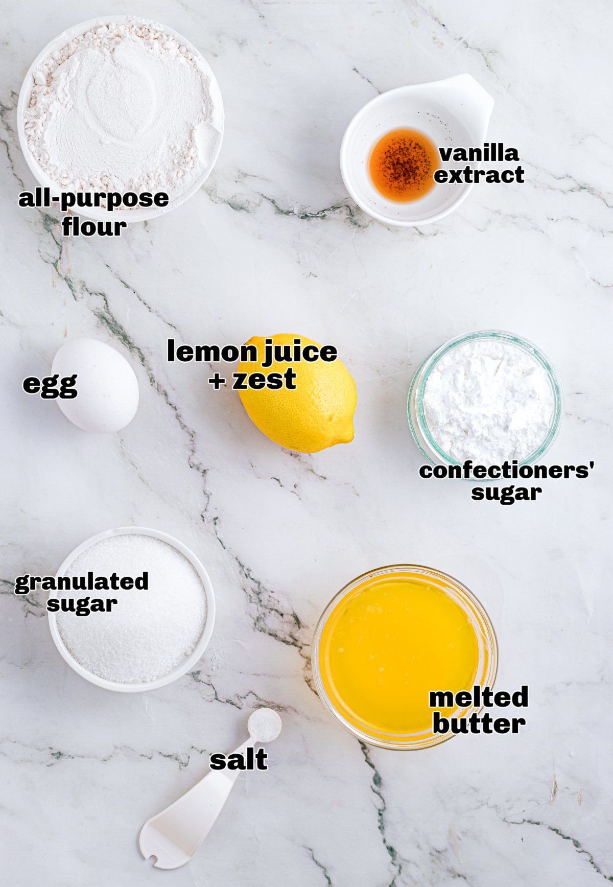 Measured baking ingredients for lemon bars laid out on a marble countertop, showing butter, sugars, lemon, egg, flour, and vanilla. Ingredients for lemon dessert bars arranged on a marble surface, including flour, sugar, melted butter, egg, lemon, vanilla extract, salt, and confectioners’ sugar.