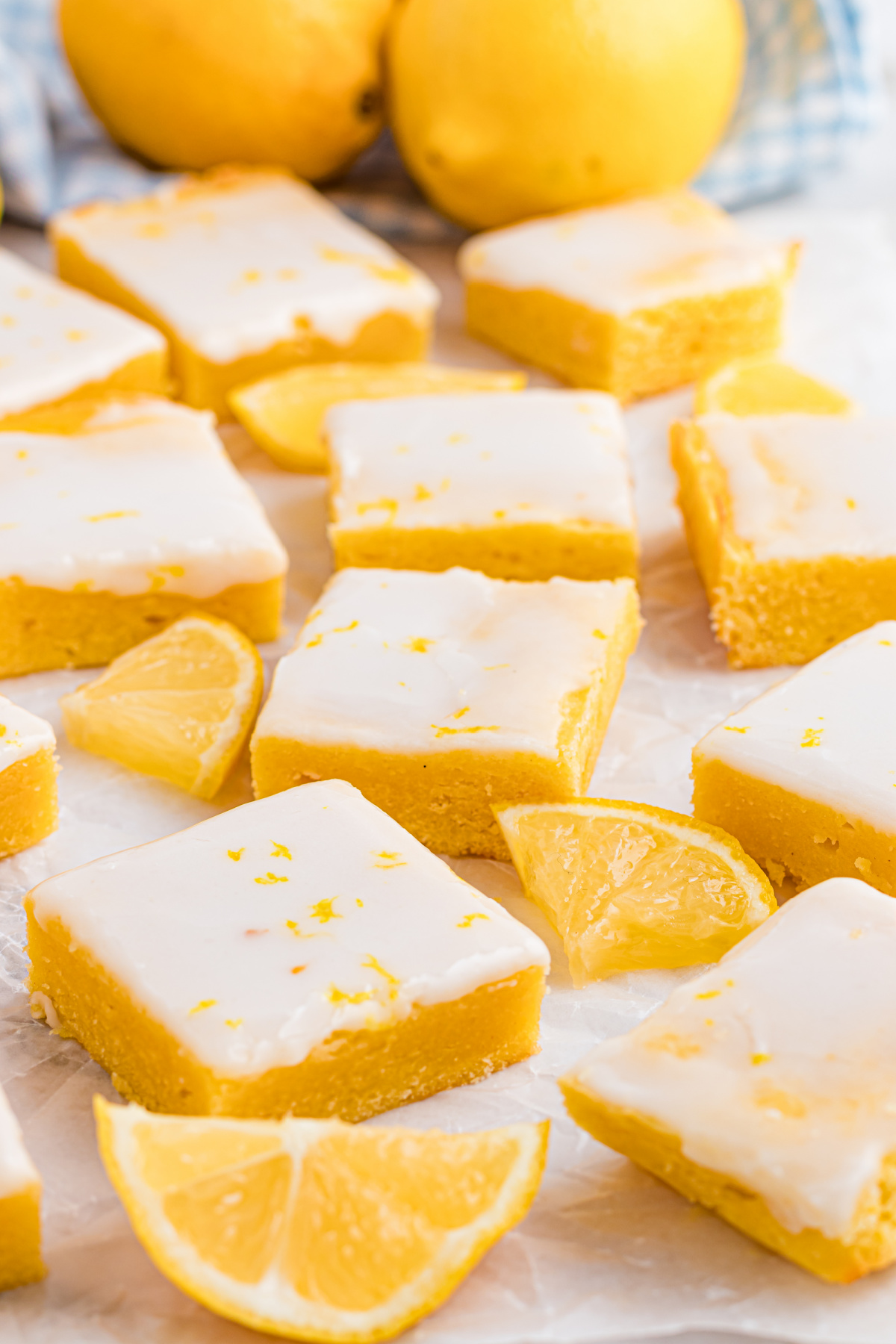 Buttery lemon blondies with fresh lemon glaze sliced into even squares, photographed on parchment with lemon wedges nearby. Lemon blondies cut into neat squares with a thin lemon glaze, showing a soft, dense crumb and clean edges on parchment paper.