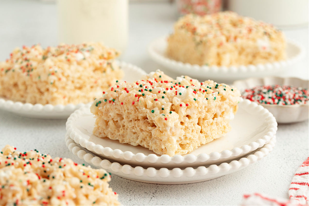 Soft sugar cookie–flavored Rice Krispie treat squares stacked on white plates with festive holiday sprinkles.