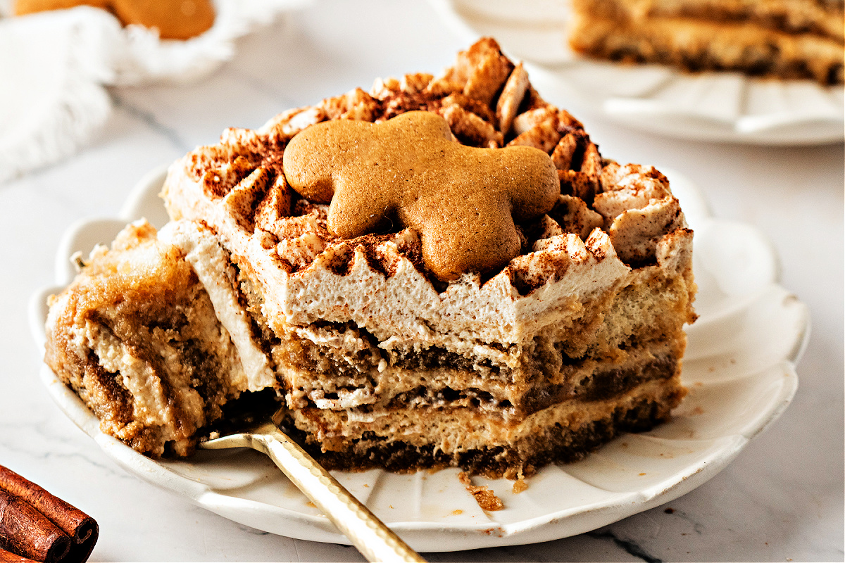 Partially eaten gingerbread tiramisu slice with layered cookies and spiced cream. A close-up slice of gingerbread tiramisu dessert on a plate, with a gingerbread cookie on top and a spoonful already taken to show the soft, spiced layers.