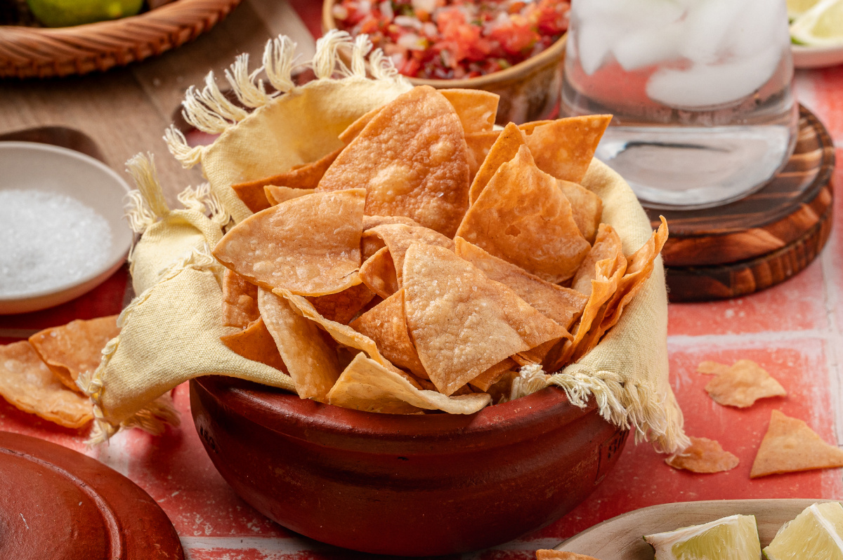 Easy fried tortilla chips piled into a rustic bowl and ready to hit the table. A rustic bowl lined with cloth and filled with easy fried tortilla chips, showing crisp edges and an even golden color ready for serving.