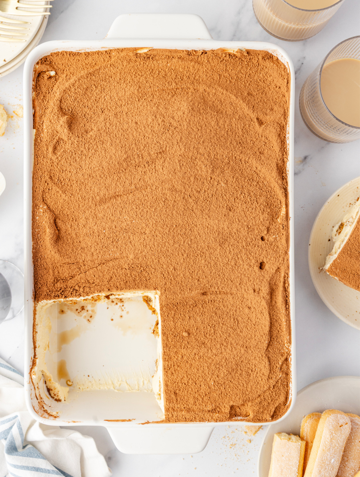 Baileys Irish Cream Tiramisu in a 9×13-inch dish with a cocoa-dusted top and a single portion removed to show the creamy mascarpone layer underneath.