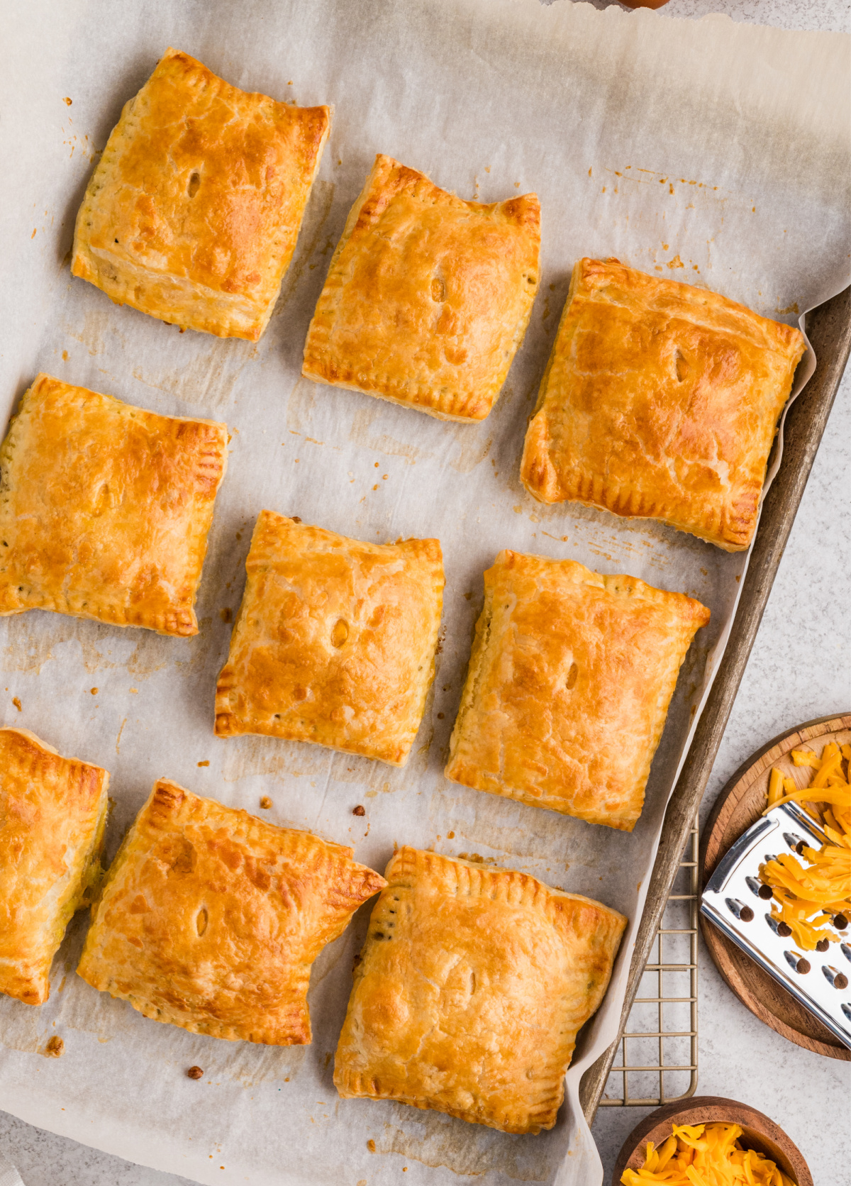 These sausage, egg, and cheese breakfast pastries come out of the oven deeply golden with crisp puff pastry layers. Flaky sausage, egg, and cheese breakfast pastries baked until golden and arranged on a parchment-lined baking sheet.