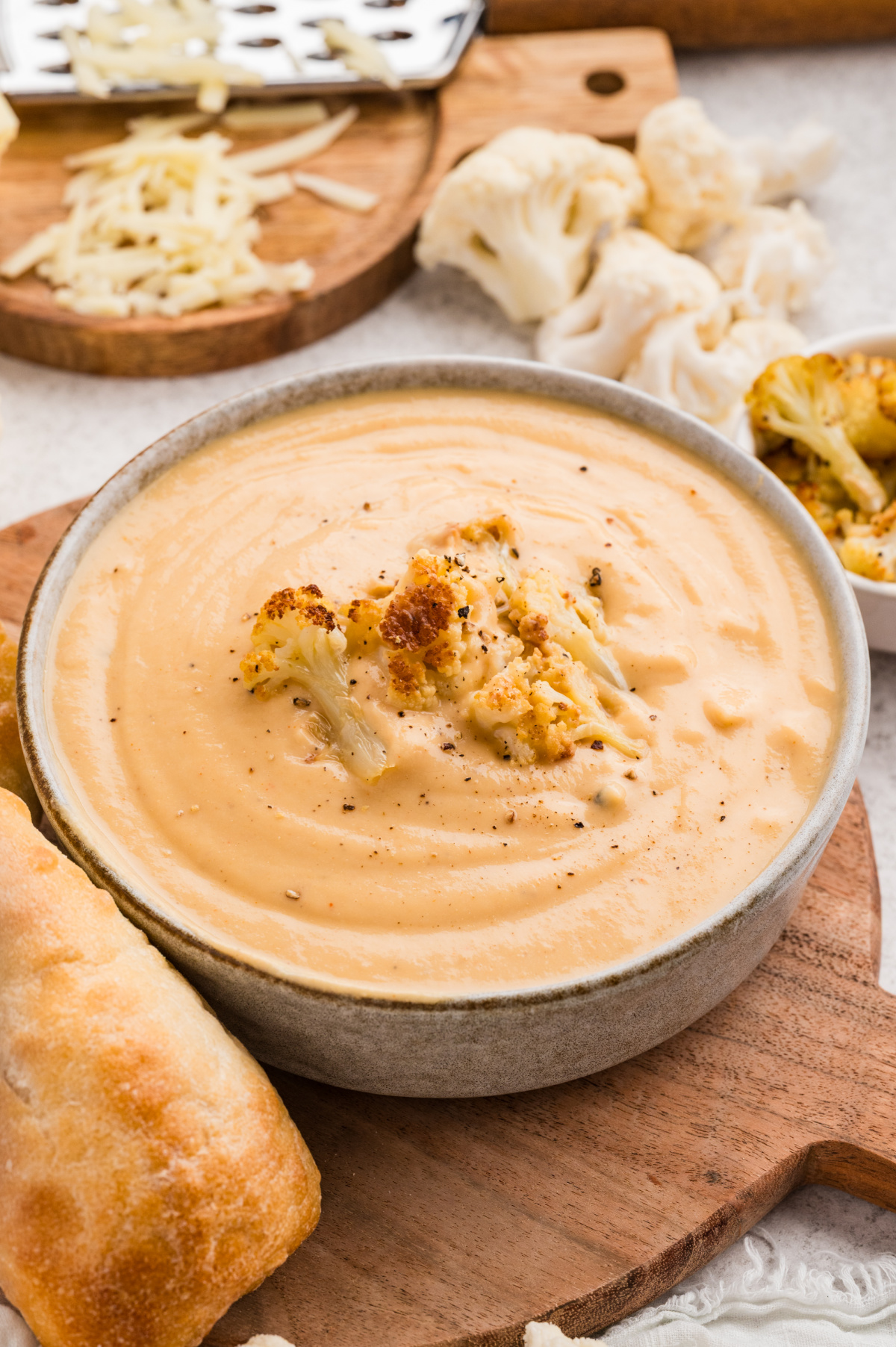 Roasted Cauliflower Soup topped with caramelized cauliflower florets and black pepper, served in a bowl with crusty bread.