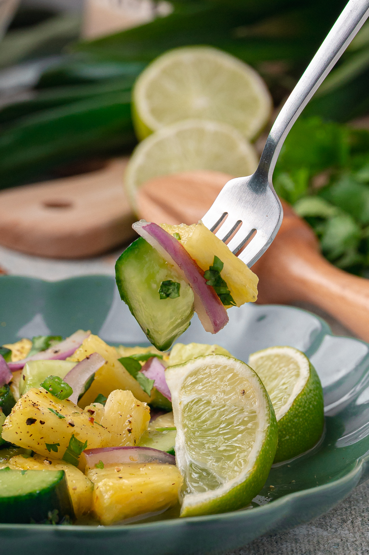 The pineapple and cucumber salad rests in a bowl ready to serve. Chilled pineapple and cucumber salad resting in a ceramic bowl with lime slices and cilantro.