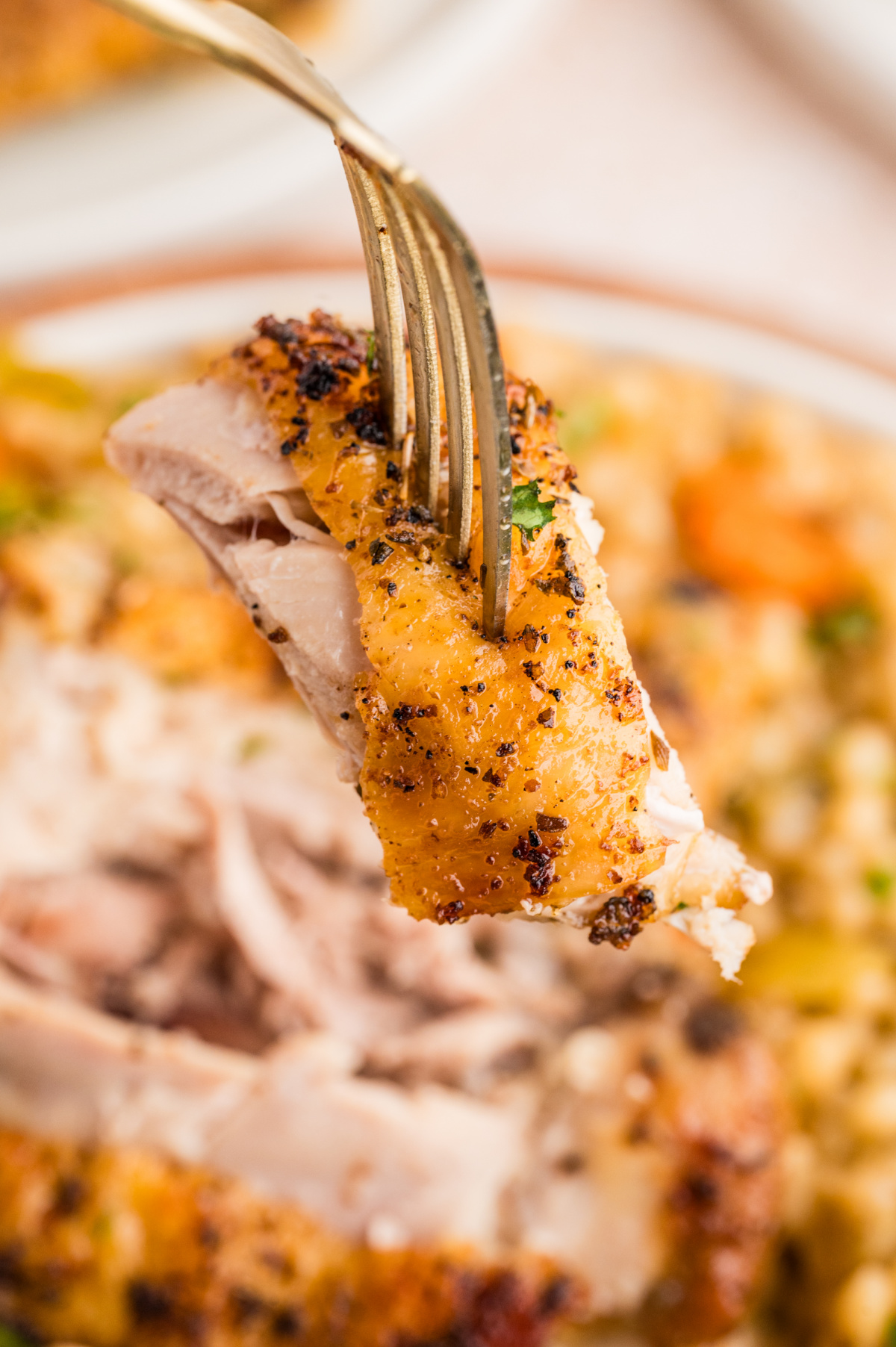 A close-up of crispy chicken thighs over pearl couscous, highlighting the crisp skin and juicy interior. Fork lifting a piece of crispy chicken thigh over pearl couscous, showing golden skin and tender meat.