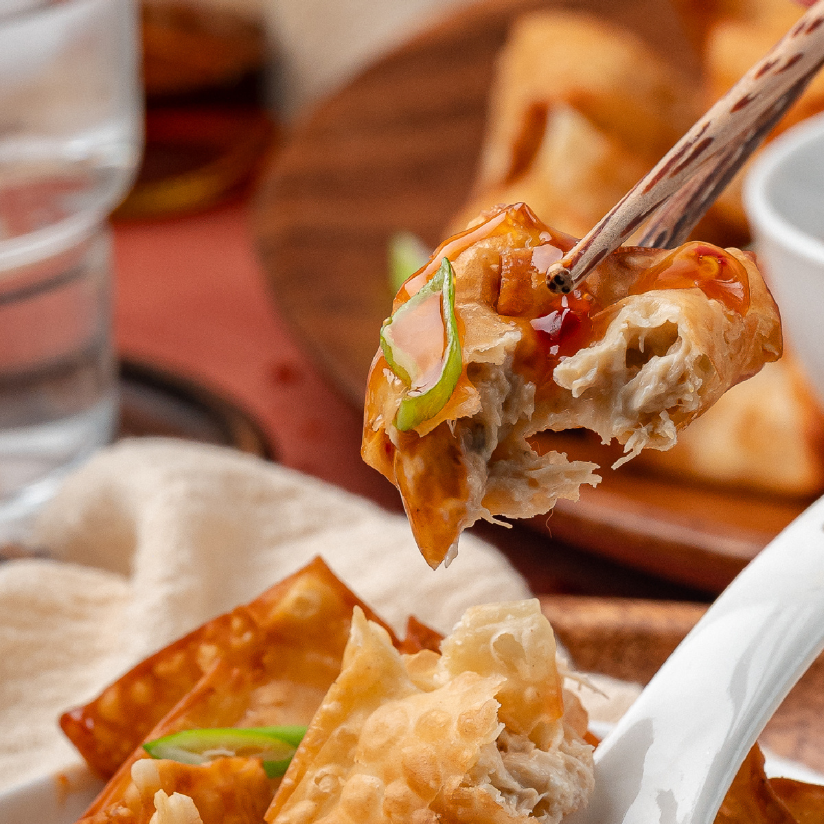 Homemade crab rangoon piled on a serving plate with crisp edges, creamy crab filling, and dipping sauce on the side.