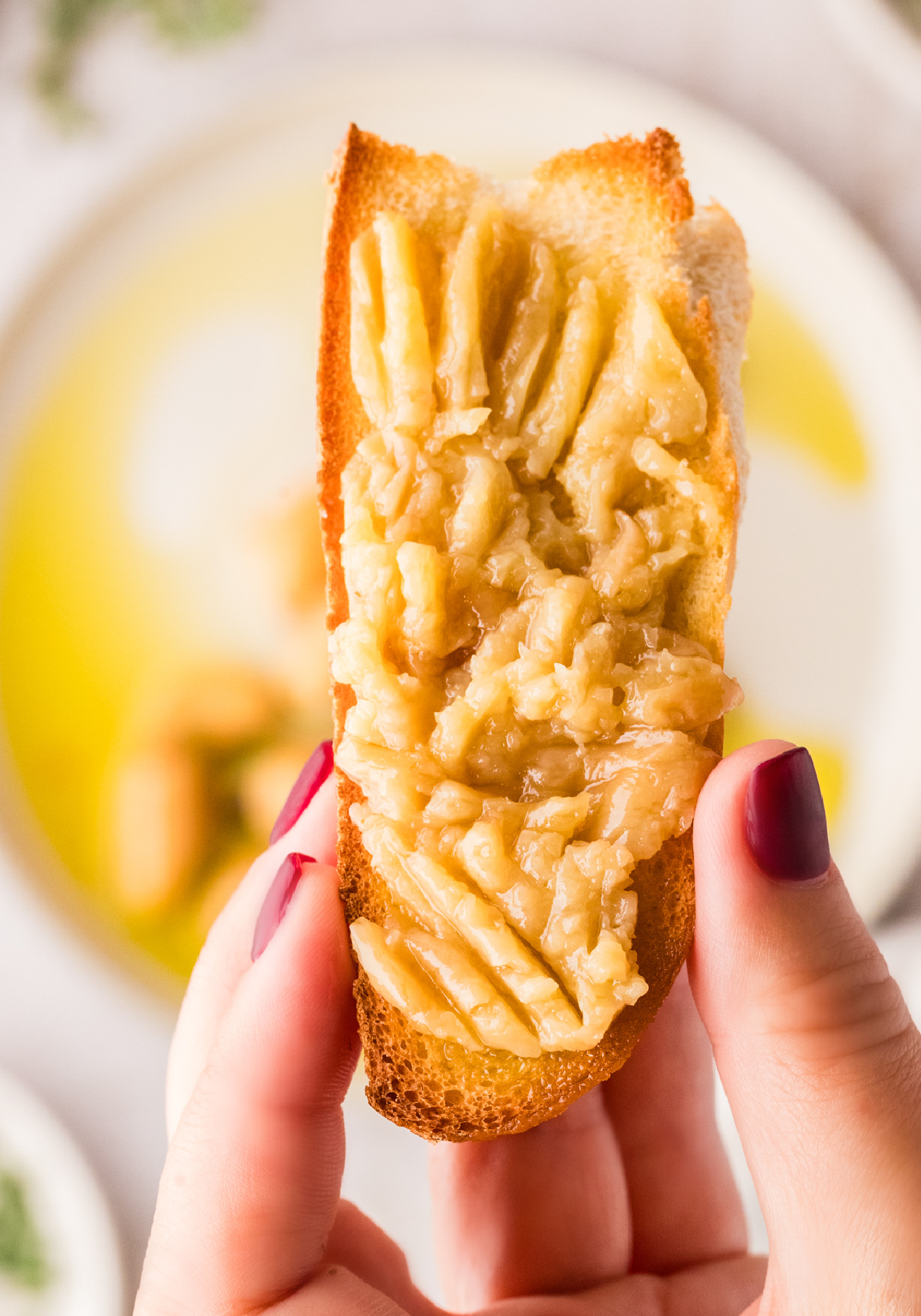 Garlic confit spread on toast with soft, oil-cooked garlic cloves. Garlic confit mashed and spread thickly onto toasted bread, shown close up.