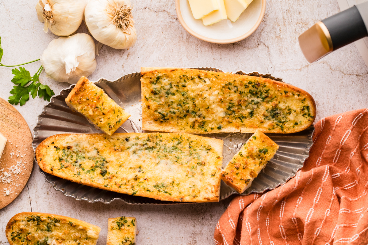 Whole pieces of garlic confit air fryer bread served crisp and golden with herbs and cheese Garlic confit air fryer bread arranged on a platter with golden tops, parsley, and Parmesan